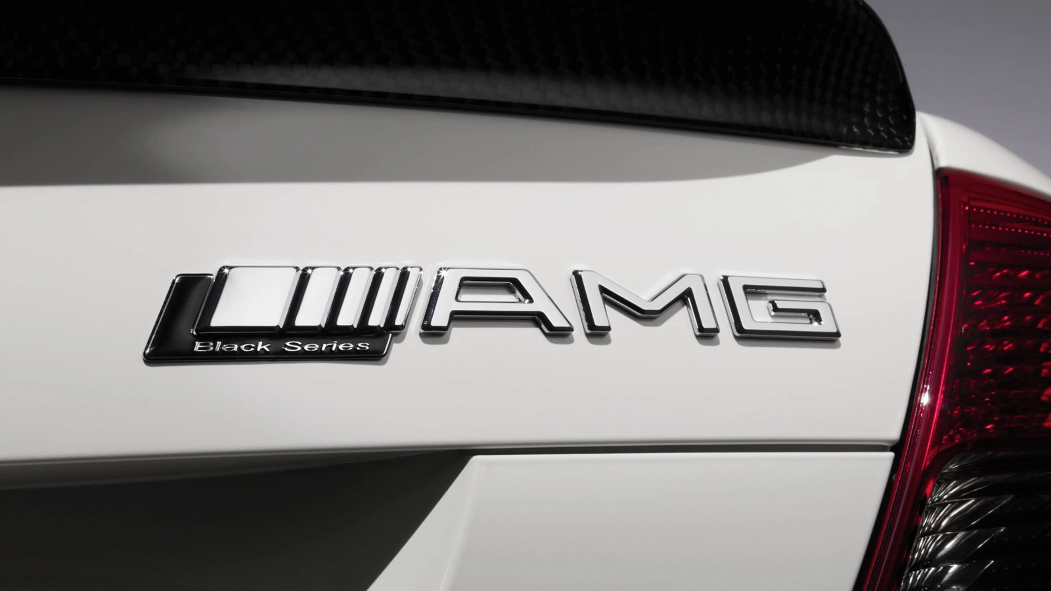 Chrome AMG Black Series badge on the rear of a white car near a red taillight and carbon fiber spoiler.