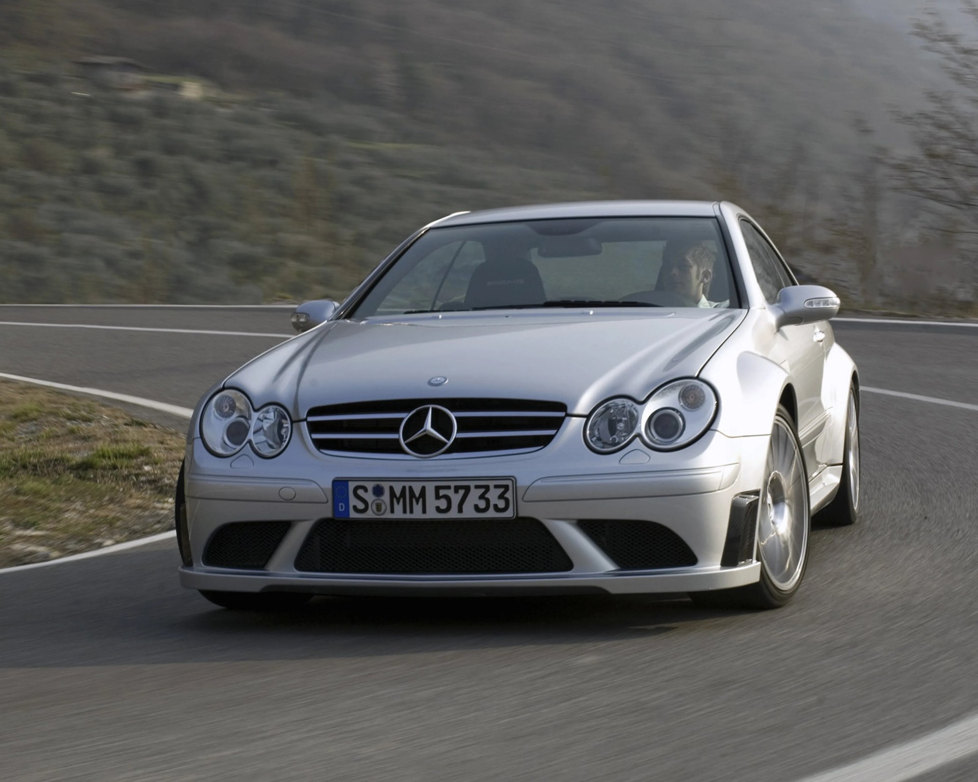 Silver Mercedes-Benz AMG coupe driving on a winding mountain road.