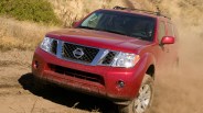 Red Nissan SUV driving on a dusty dirt road with dry grass in the background.