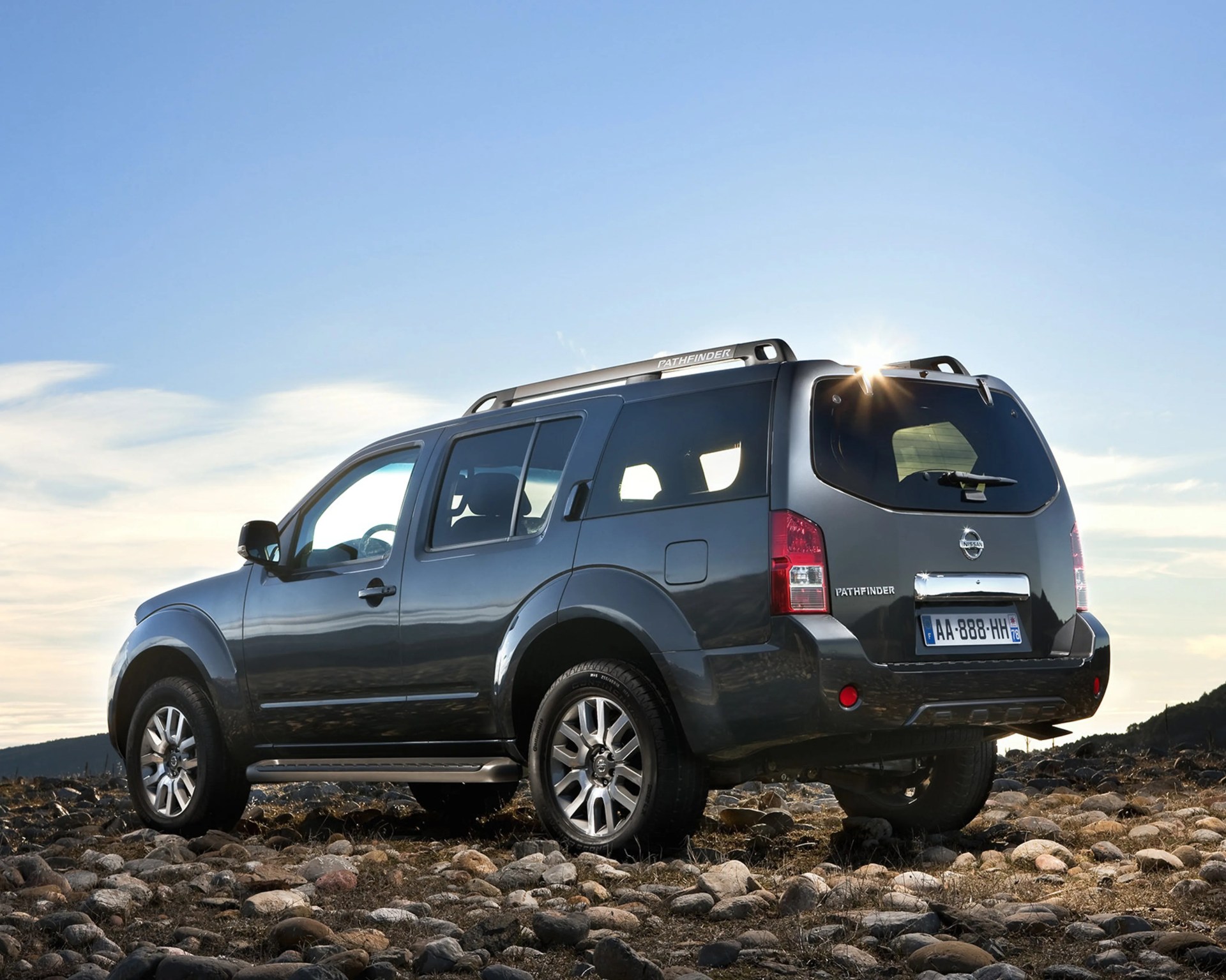 Dark gray Nissan Pathfinder SUV parked on rocky terrain with clear sky in the background.