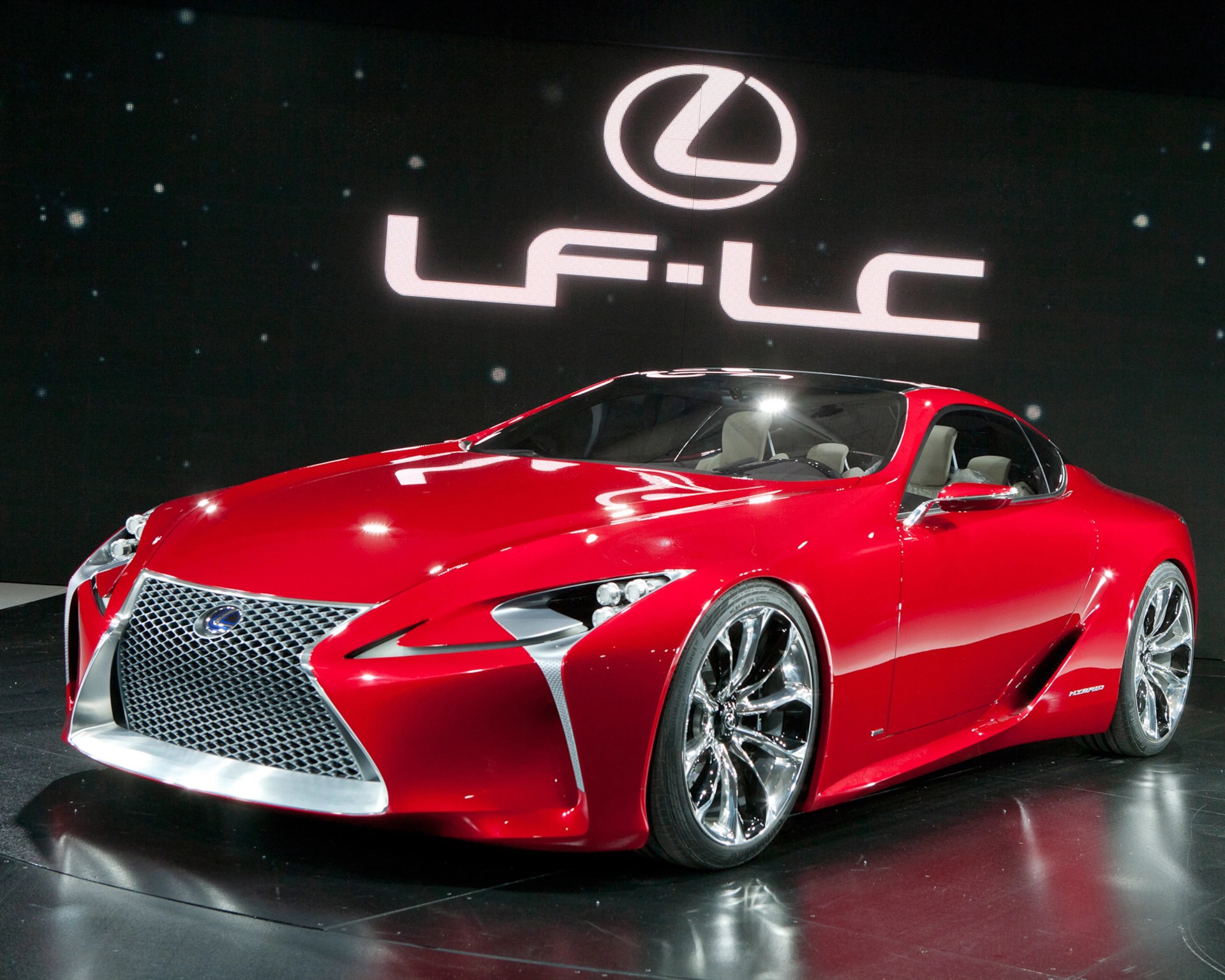 Red Lexus LF-LC hybrid sports car with large chrome grille and wheels on display stage.