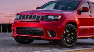 Front side view of a red Jeep Grand Cherokee with black grille and black wheels on a paved surface.