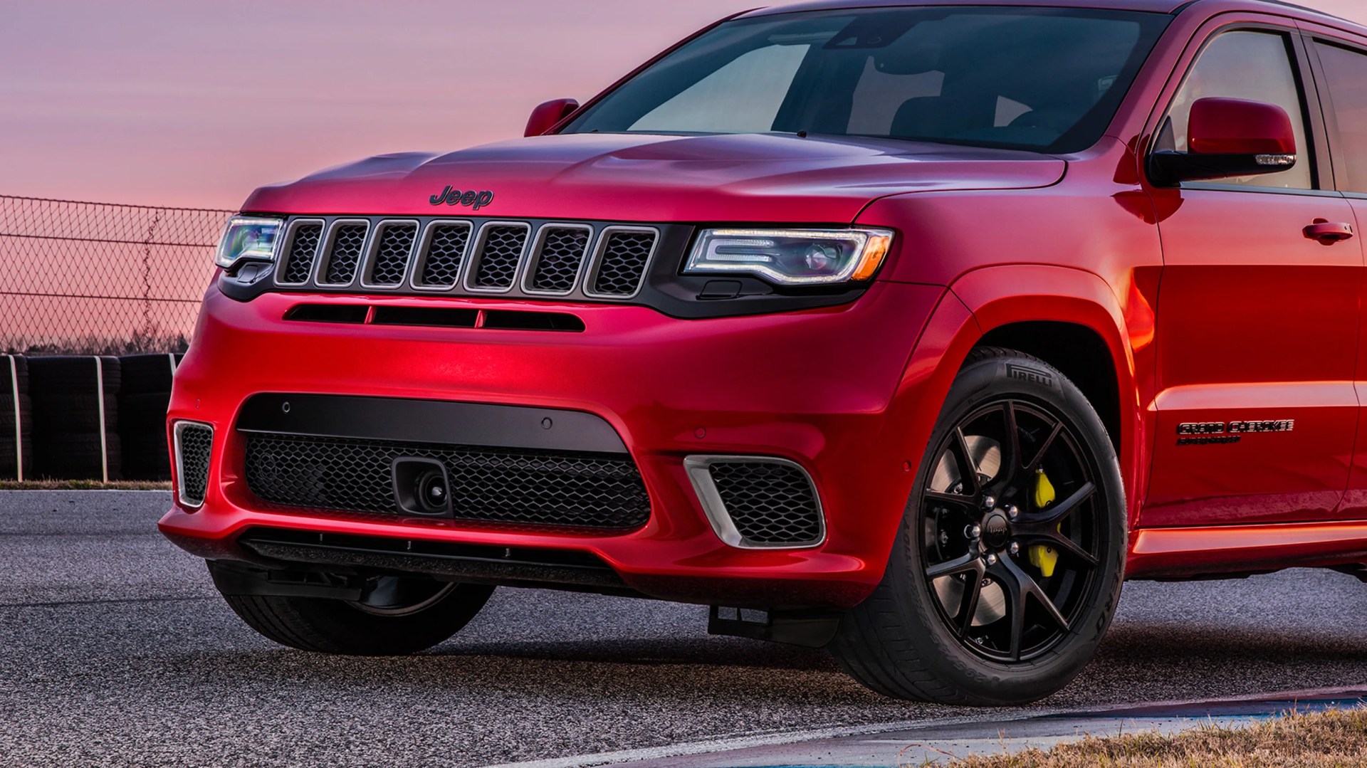 Front side view of a red Jeep Grand Cherokee with black grille and black wheels on a paved surface.