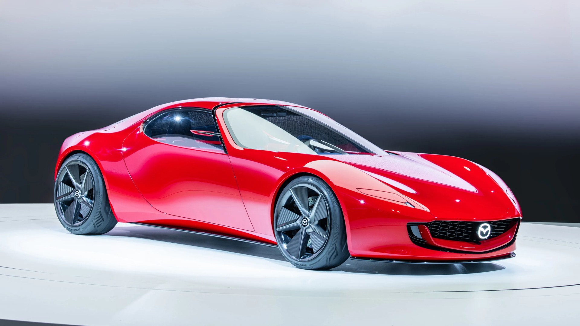 Red sleek Mazda sports car with black aerodynamic wheels on a white platform.