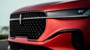 Front grille and headlight of a red Lincoln vehicle with a black mesh pattern and chrome emblem.