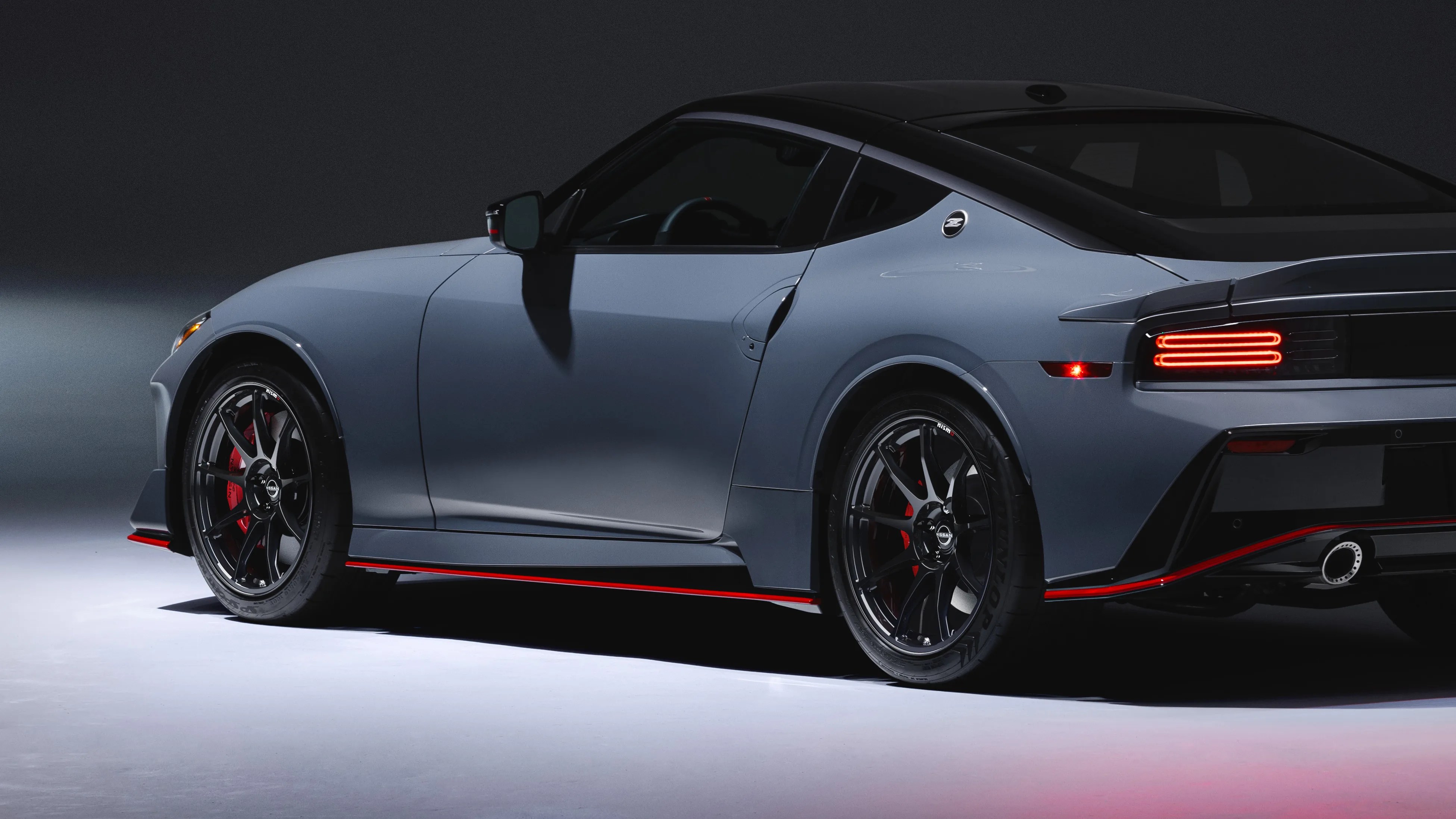 Matte gray Nissan sports car with black roof, black wheels, red brake calipers, and red trim accents.