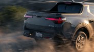 Rear view of a gray Hyundai Santa Cruz 2.5T pickup truck kicking up dust on a dirt road.