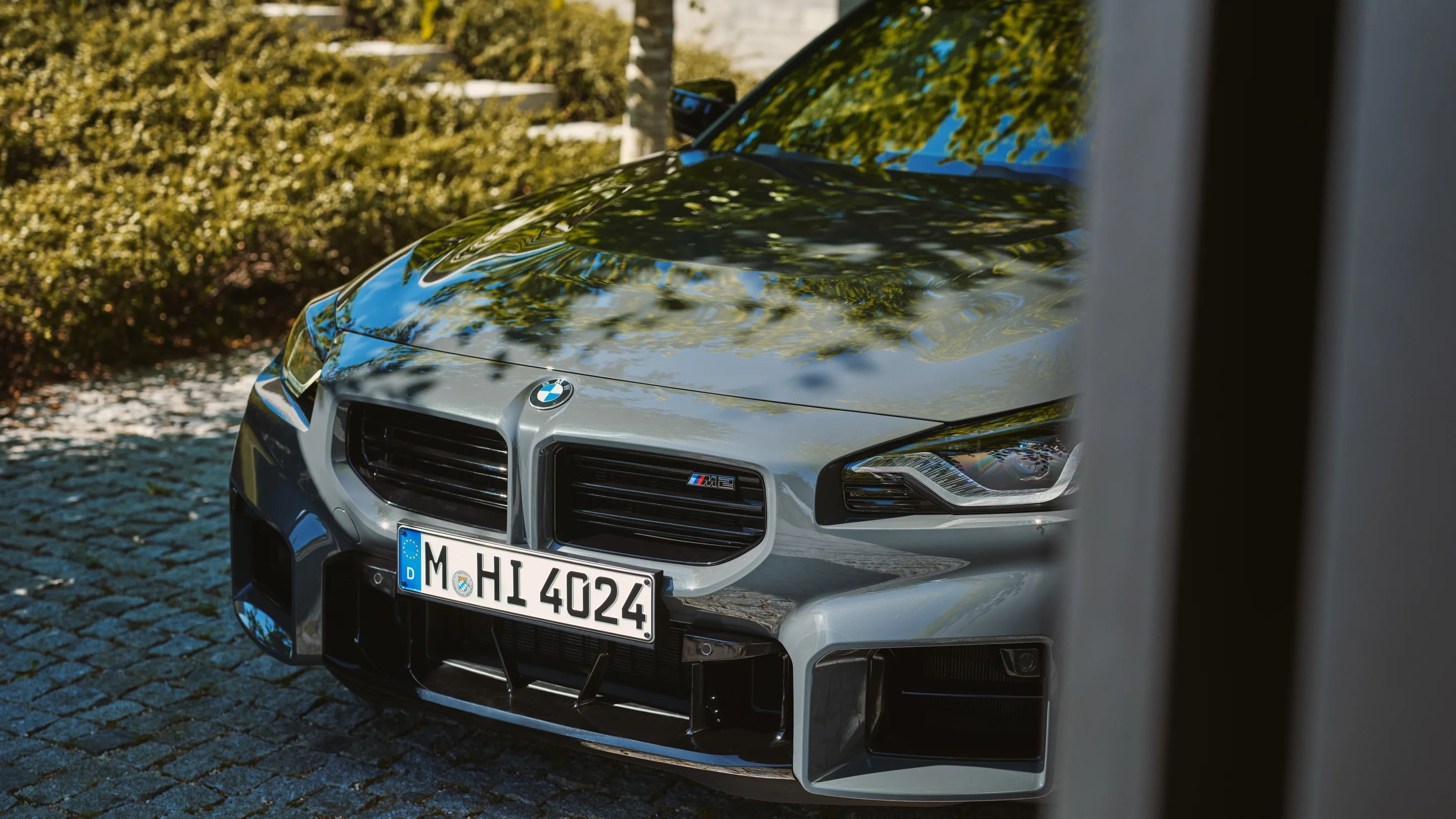 Front view of a gray BMW M2 with a German license plate parked on a cobblestone surface.