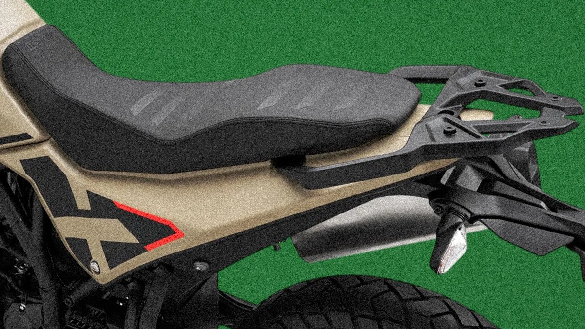 Close-up of a black and tan motorcycle seat with a rear luggage rack and knobby tire against a green background.