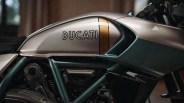 Silver Ducati motorcycle fuel tank with a gold vertical stripe and green frame parts.