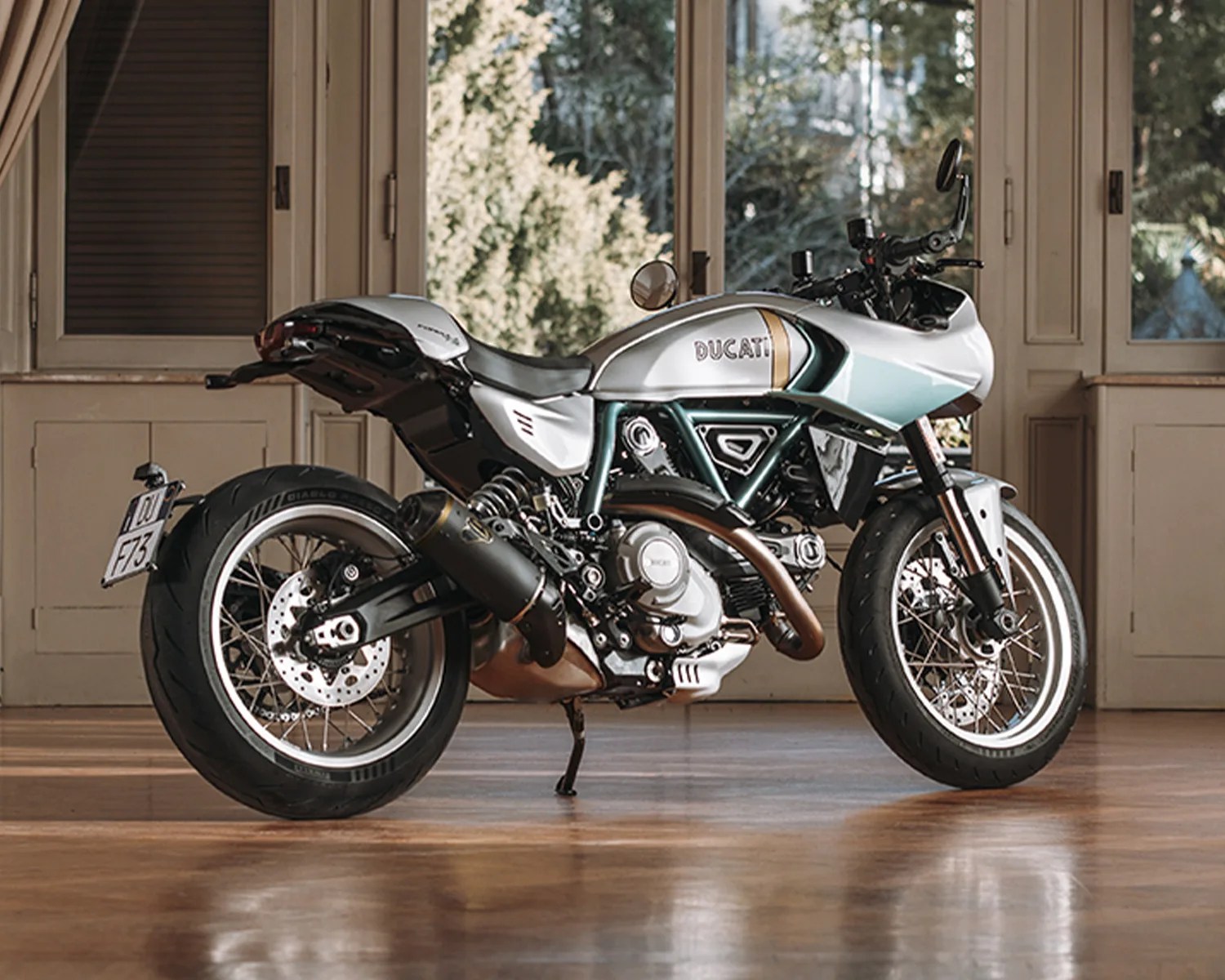 Silver and black Ducati motorcycle with spoked wheels parked indoors on a wooden floor.