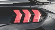Close-up of a black car's rear with three red, angular tail lights in a row.
