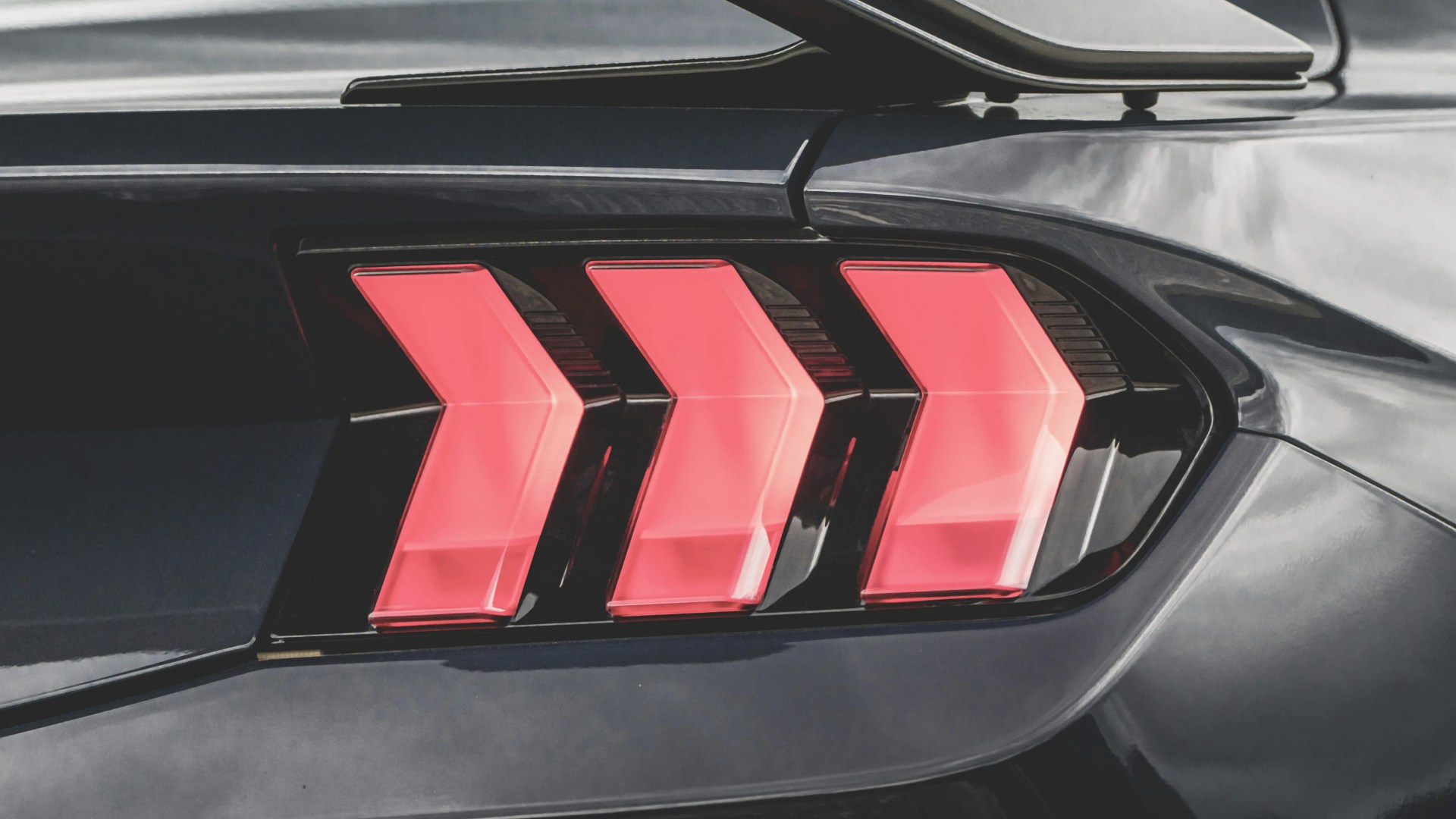 Close-up of a black car's rear with three red, angular tail lights in a row.