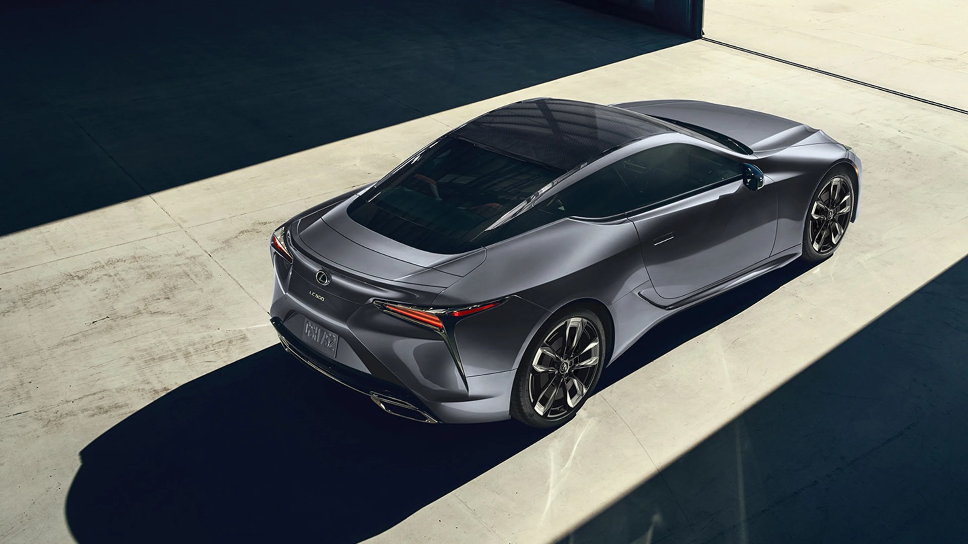 Gray Lexus LC 500 sports coupe parked indoors with sunlight casting shadows on the floor.