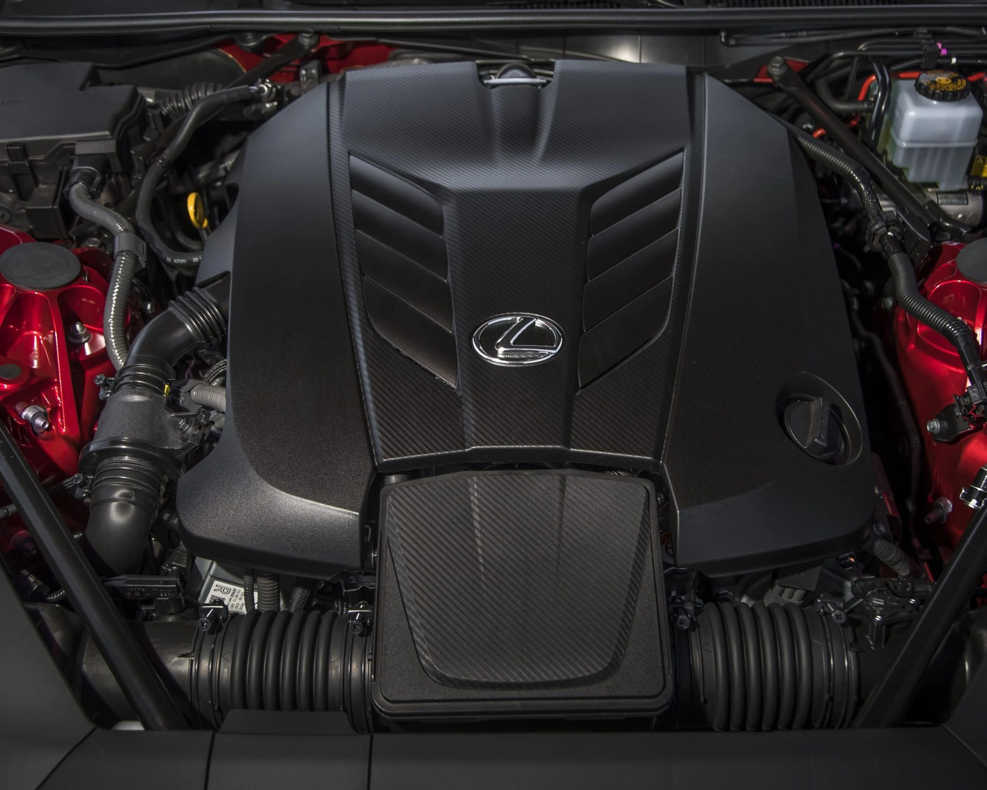 Lexus engine bay with black carbon fiber engine cover and red metallic components.