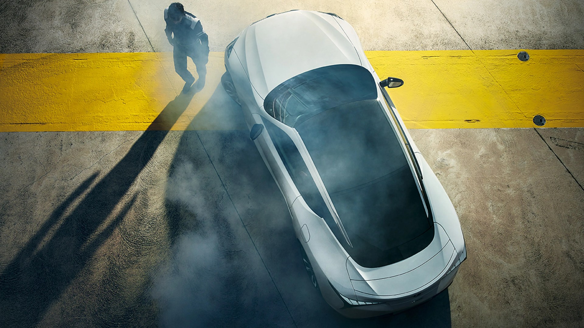 White sports car with tinted windows on concrete near a wide yellow line, with smoke and a person casting a long shadow nearby.
