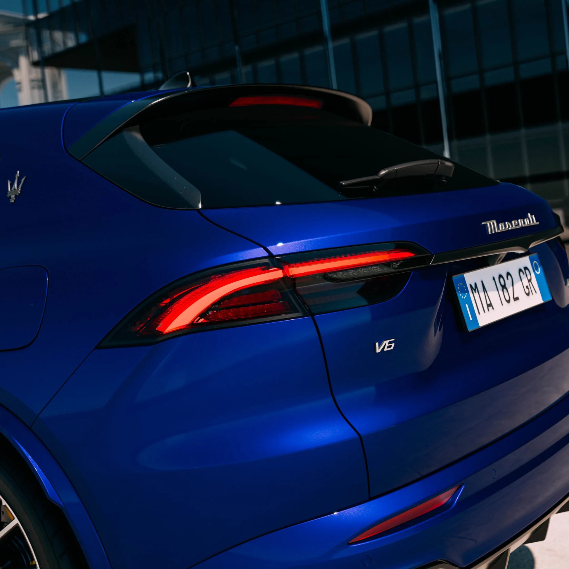 Rear view of a blue Maserati SUV showing the V6 badge, taillight, and Italian license plate.