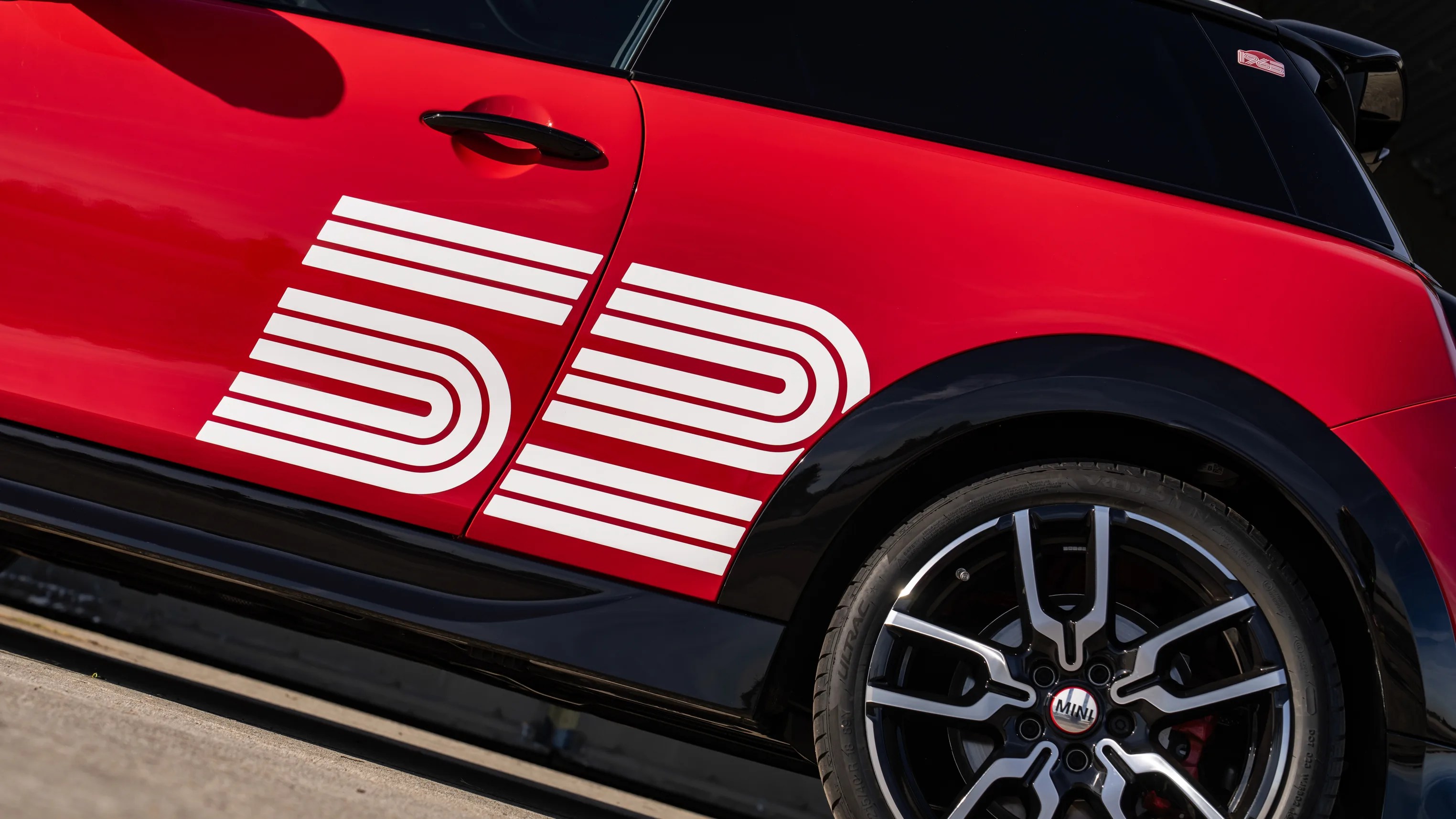 Red Mini Cooper with white "52" decal on the door and black wheel arches and alloy wheels.