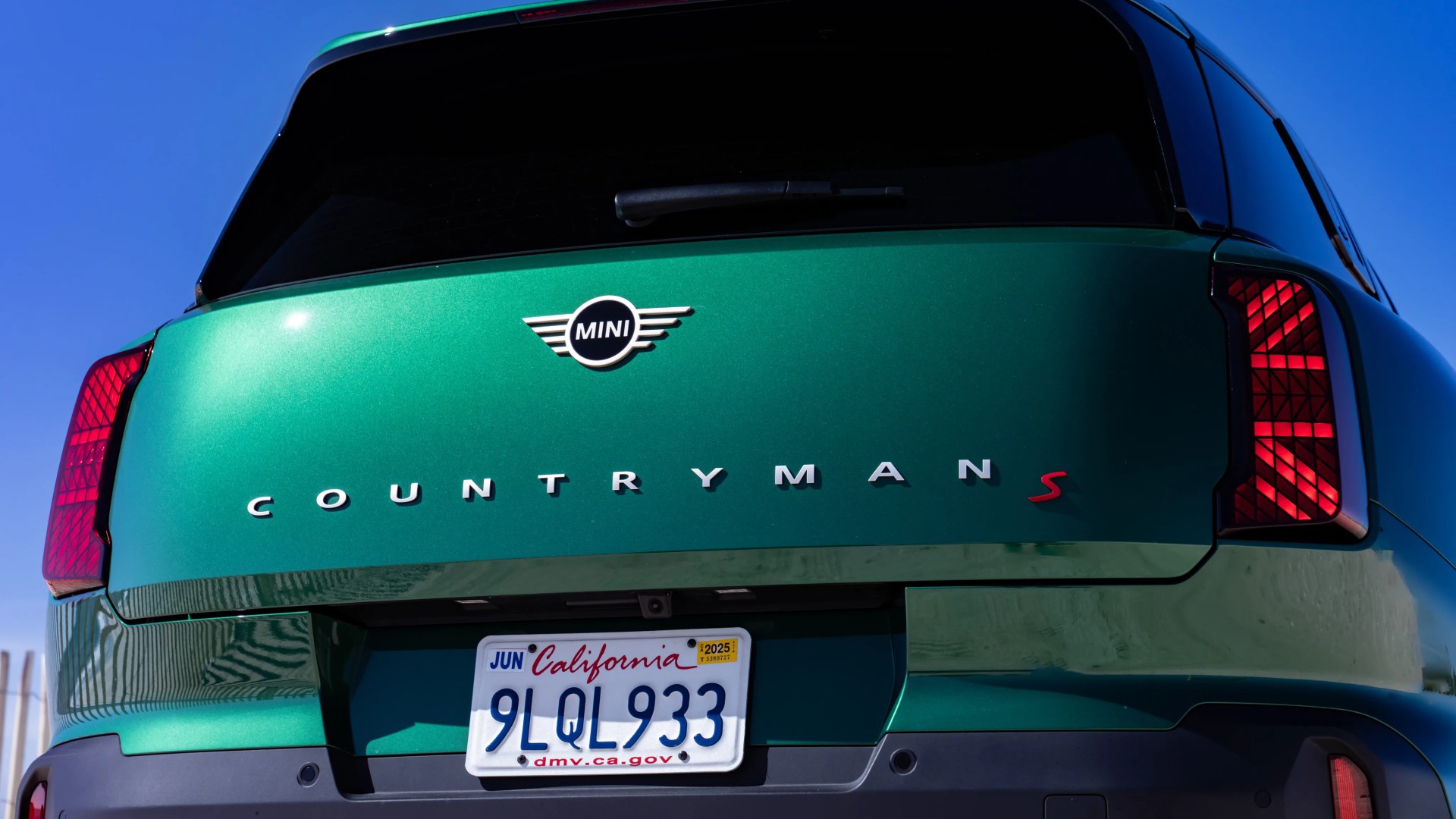 Rear view of a green Mini Countryman S with California license plate 9LQL933 under a clear blue sky.