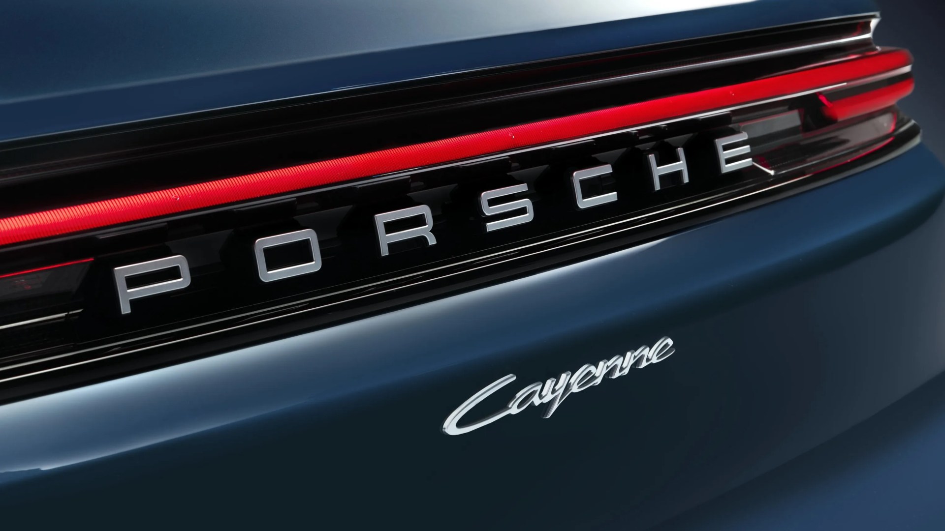 Rear view of a dark blue Porsche Cayenne showing the Porsche logo and red tail light strip.