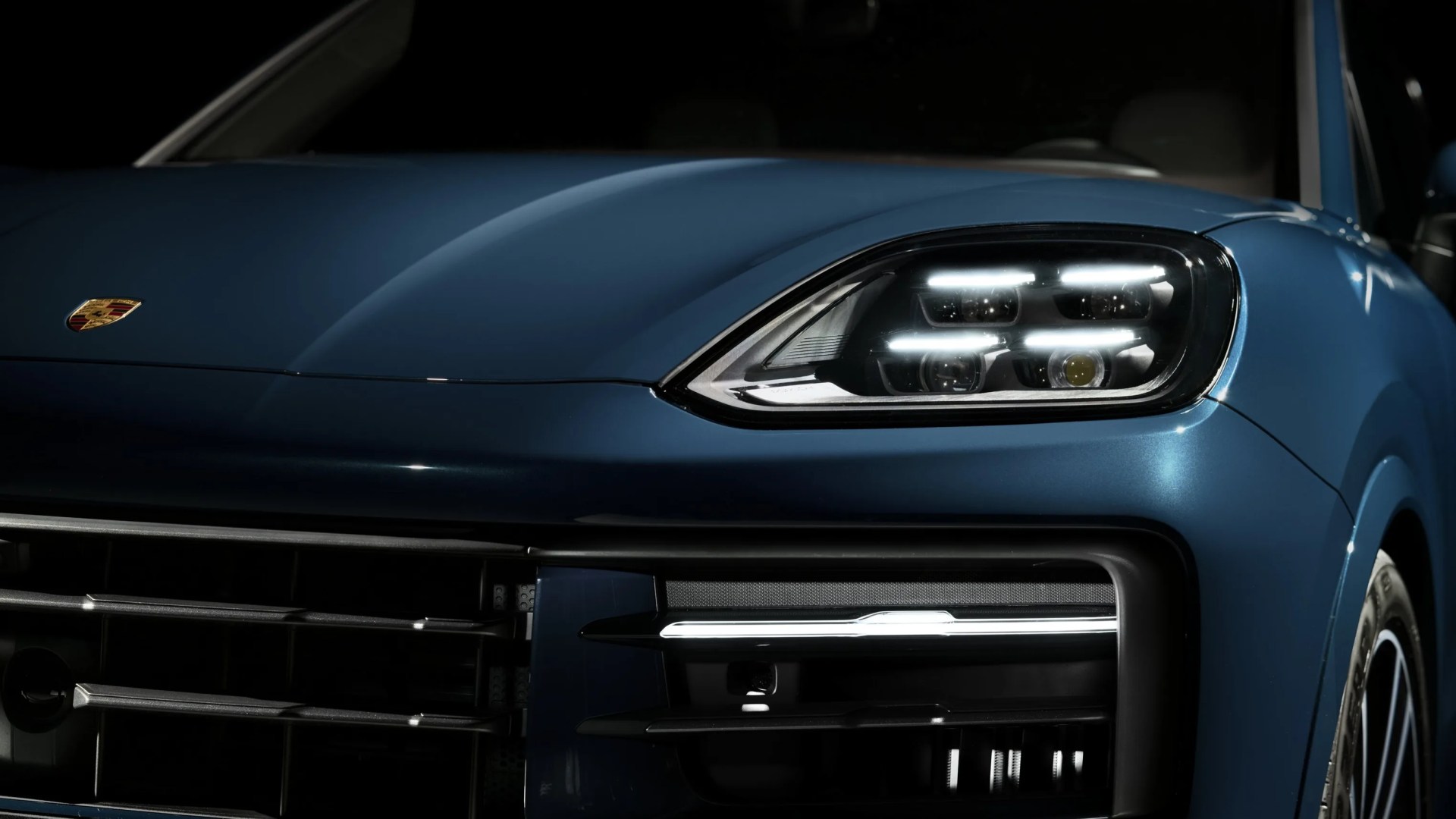 Front right headlight and grille of a blue Porsche car with illuminated LED lights.