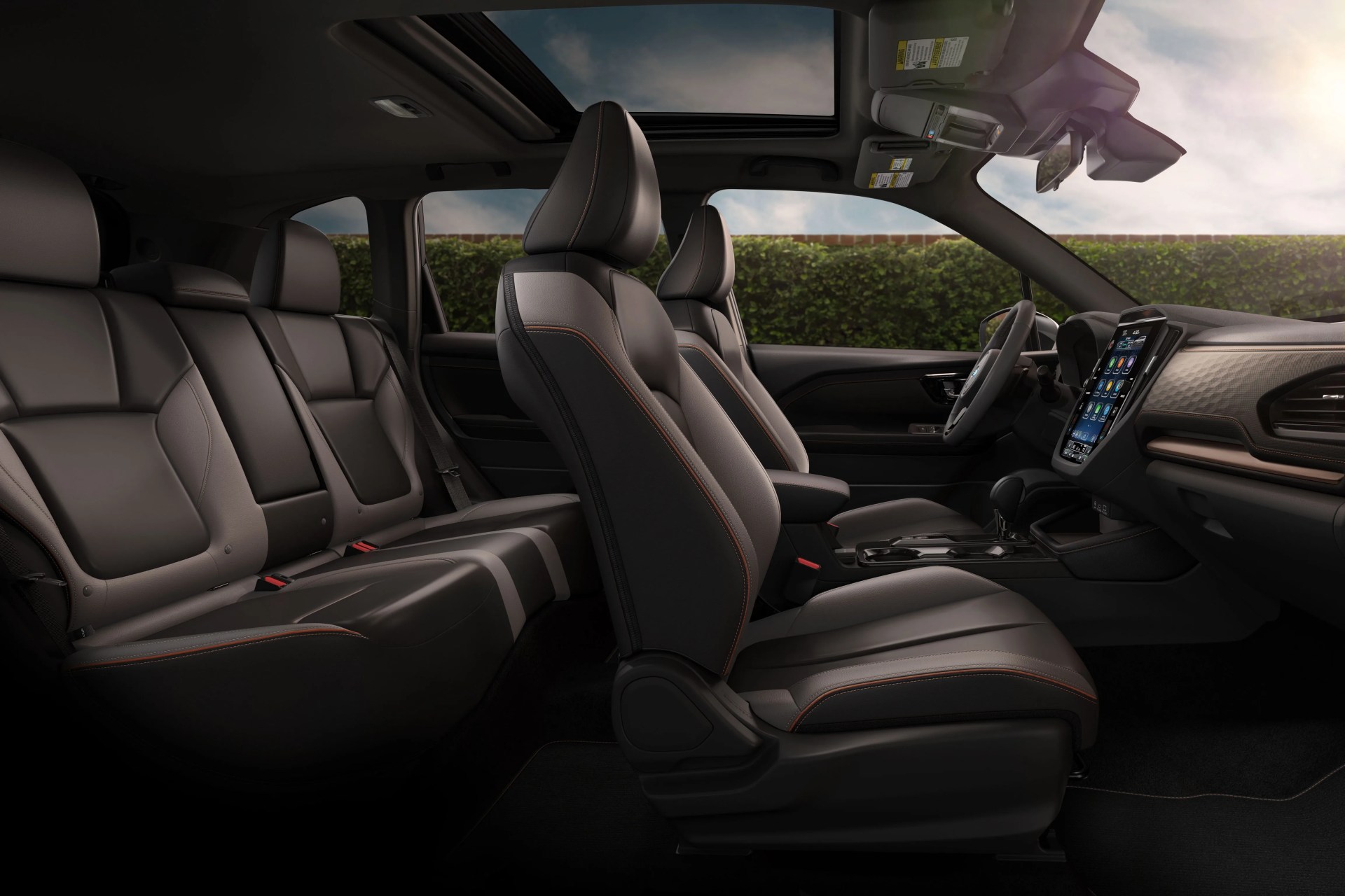 Car interior with black and gray leather seats, orange stitching, panoramic sunroof, and a large touchscreen display on the dashboard.