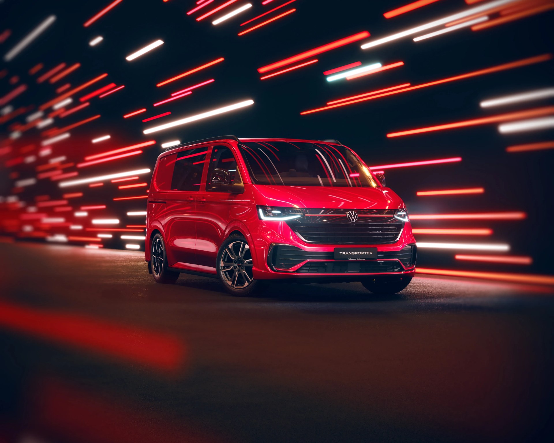 Red Volkswagen Transporter van with black grille and alloy wheels against a dark background with red and white light streaks.