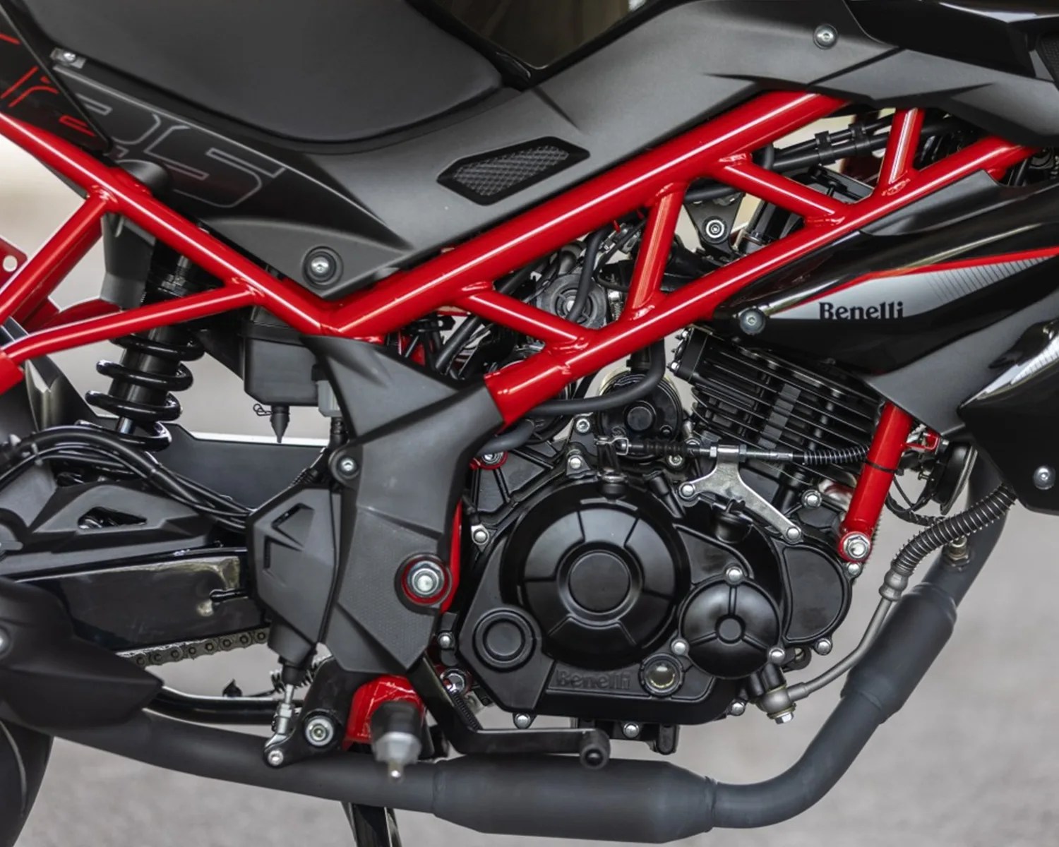 Close-up of a black and red Benelli motorcycle engine and frame with visible exhaust pipe and suspension.