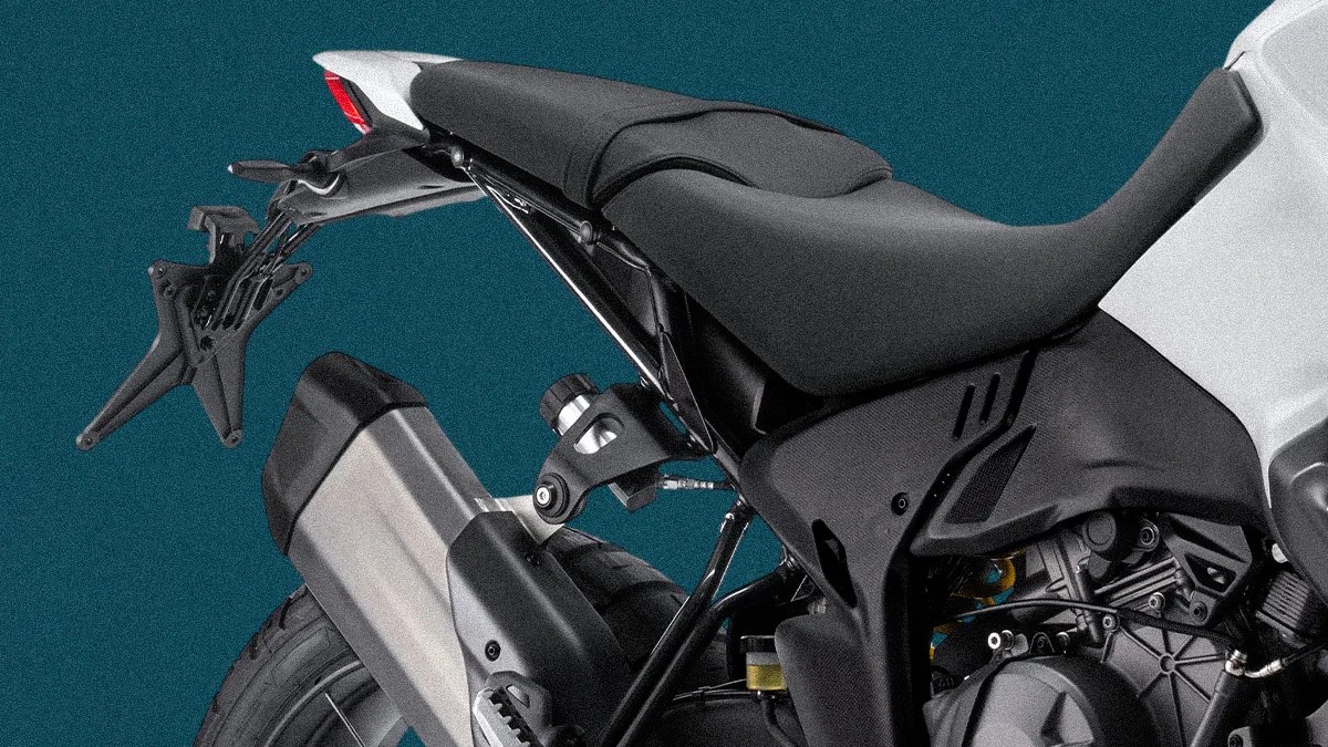 Rear section of a black and white motorcycle showing the seat, exhaust pipe, and rear tire against a teal background.