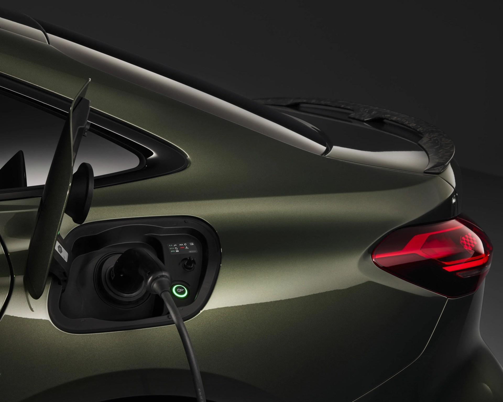 Dark green electric car rear side with charging cable plugged in and red taillight.