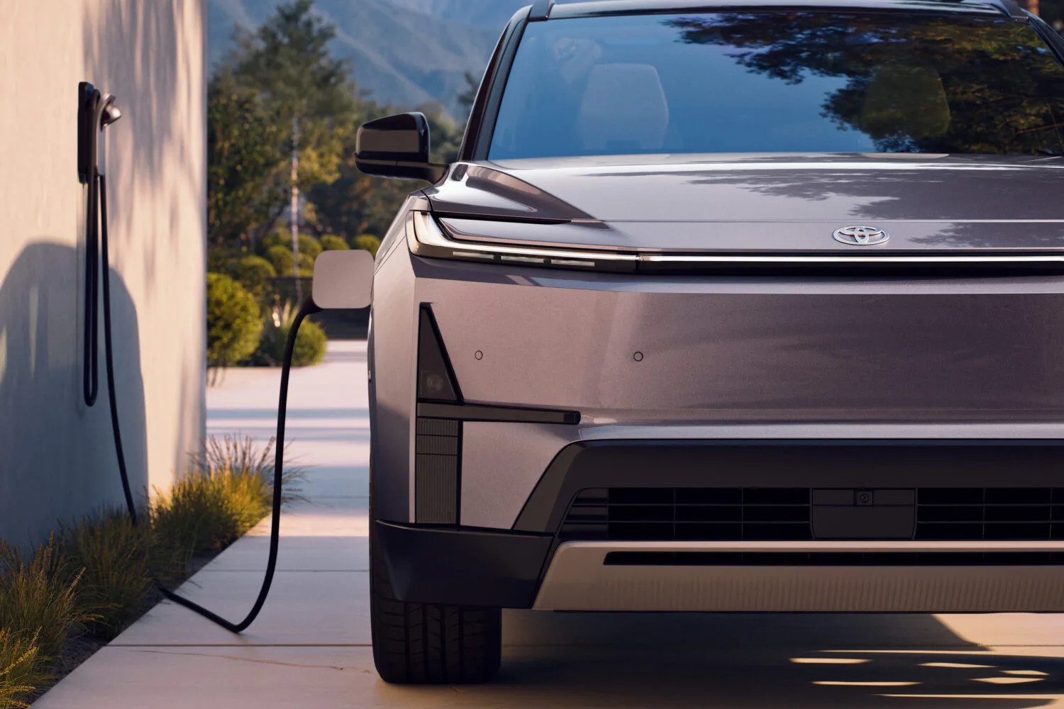 Front view of a silver Toyota electric vehicle plugged into a wall charger outdoors.