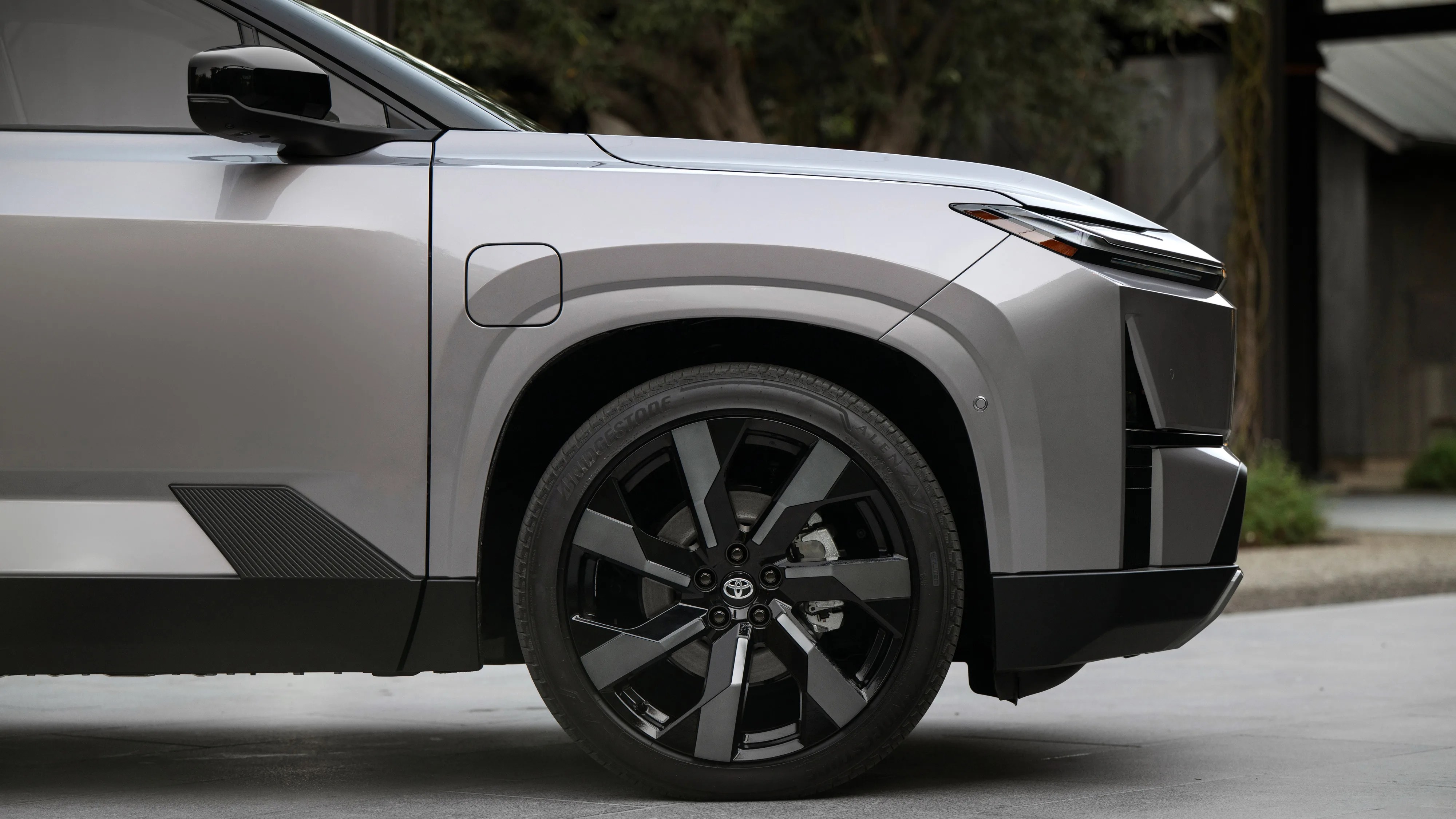 Close-up of the front left side of a silver Toyota vehicle showing a black alloy wheel and side mirror.