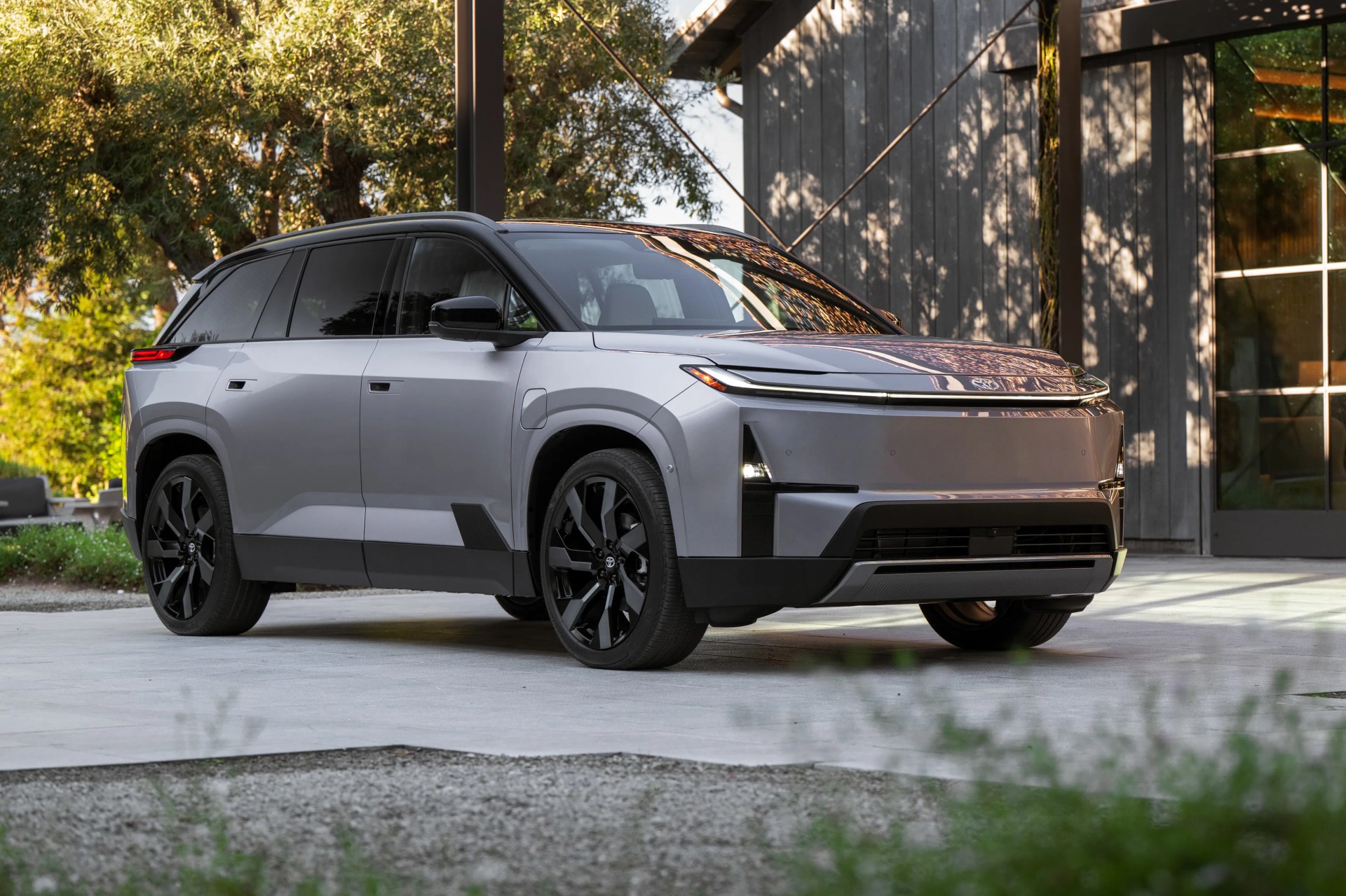 Silver electric SUV with black roof and wheels parked on a concrete driveway near a modern building.