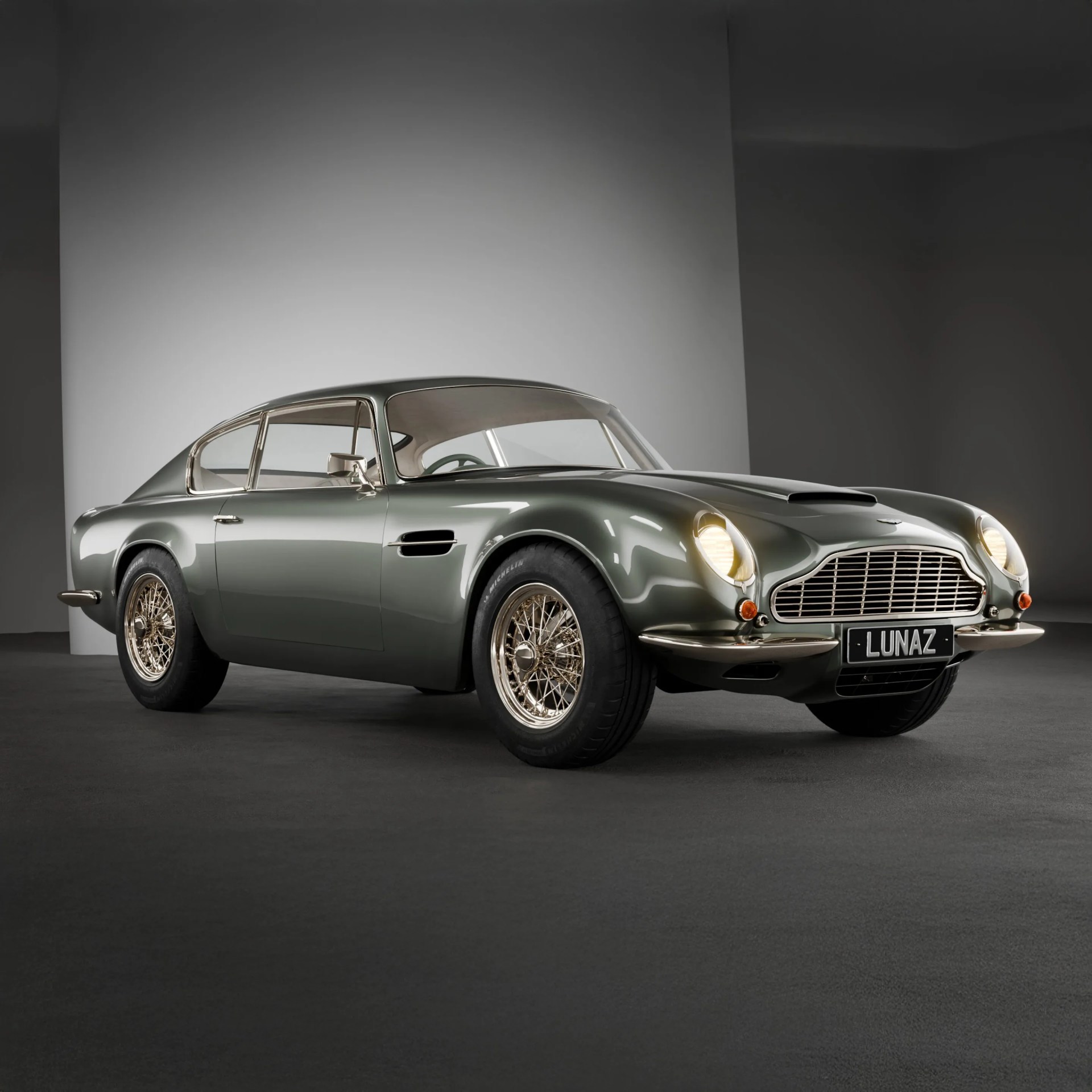Dark green classic Aston Martin car with gold wire-spoke wheels and headlights on in a studio.
