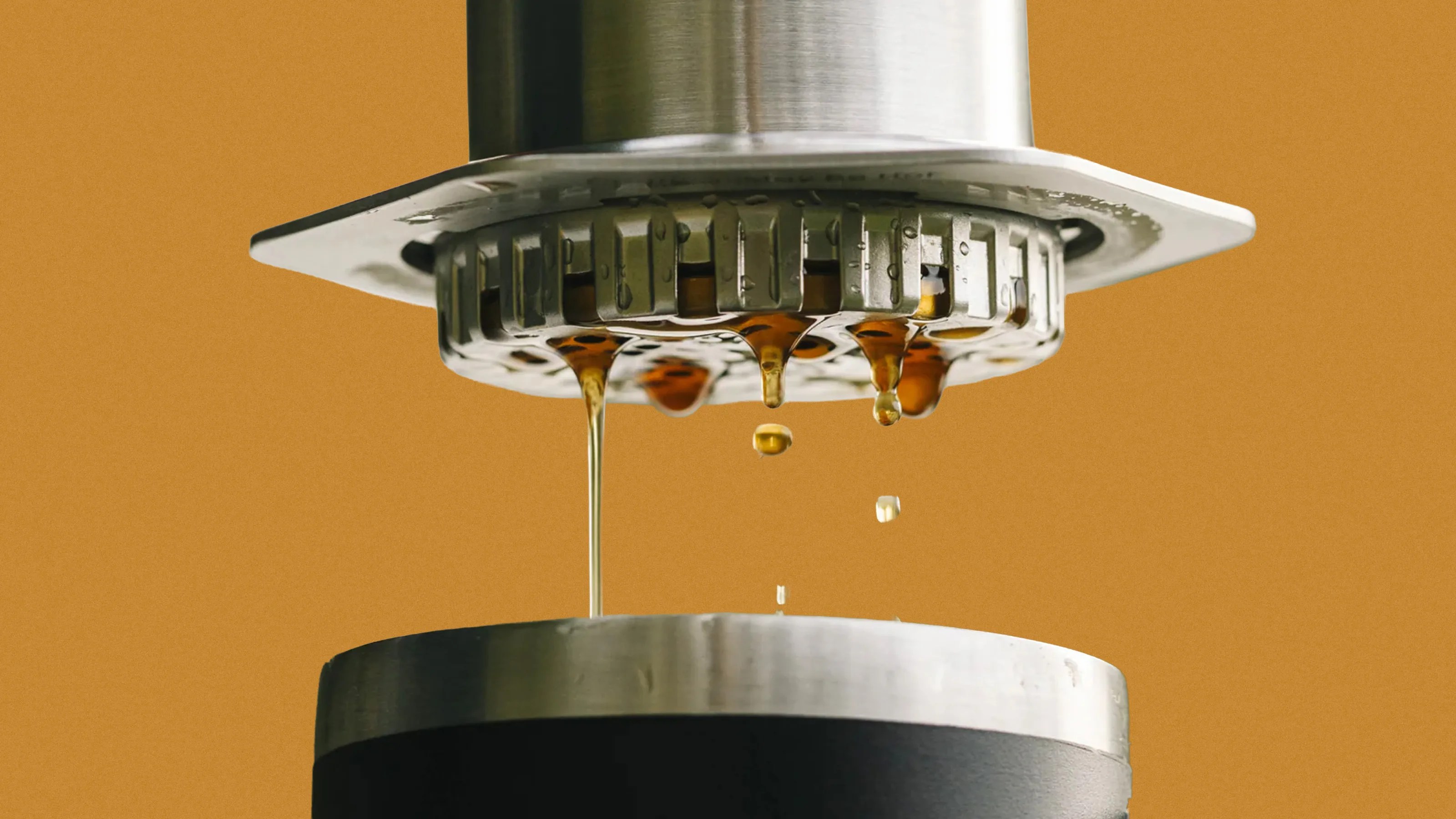 Close-up of espresso machine portafilter dripping dark coffee into a metal cup against a brown background.