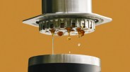 Close-up of espresso machine portafilter dripping dark coffee into a metal cup against a brown background.