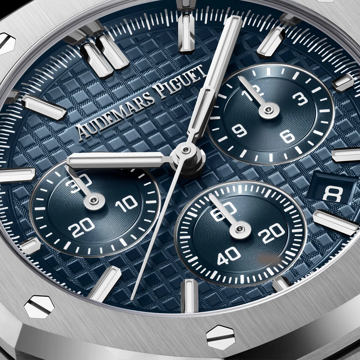 Close-up of a blue Audemars Piguet watch dial with silver hands, subdials, and a brushed stainless steel bezel.