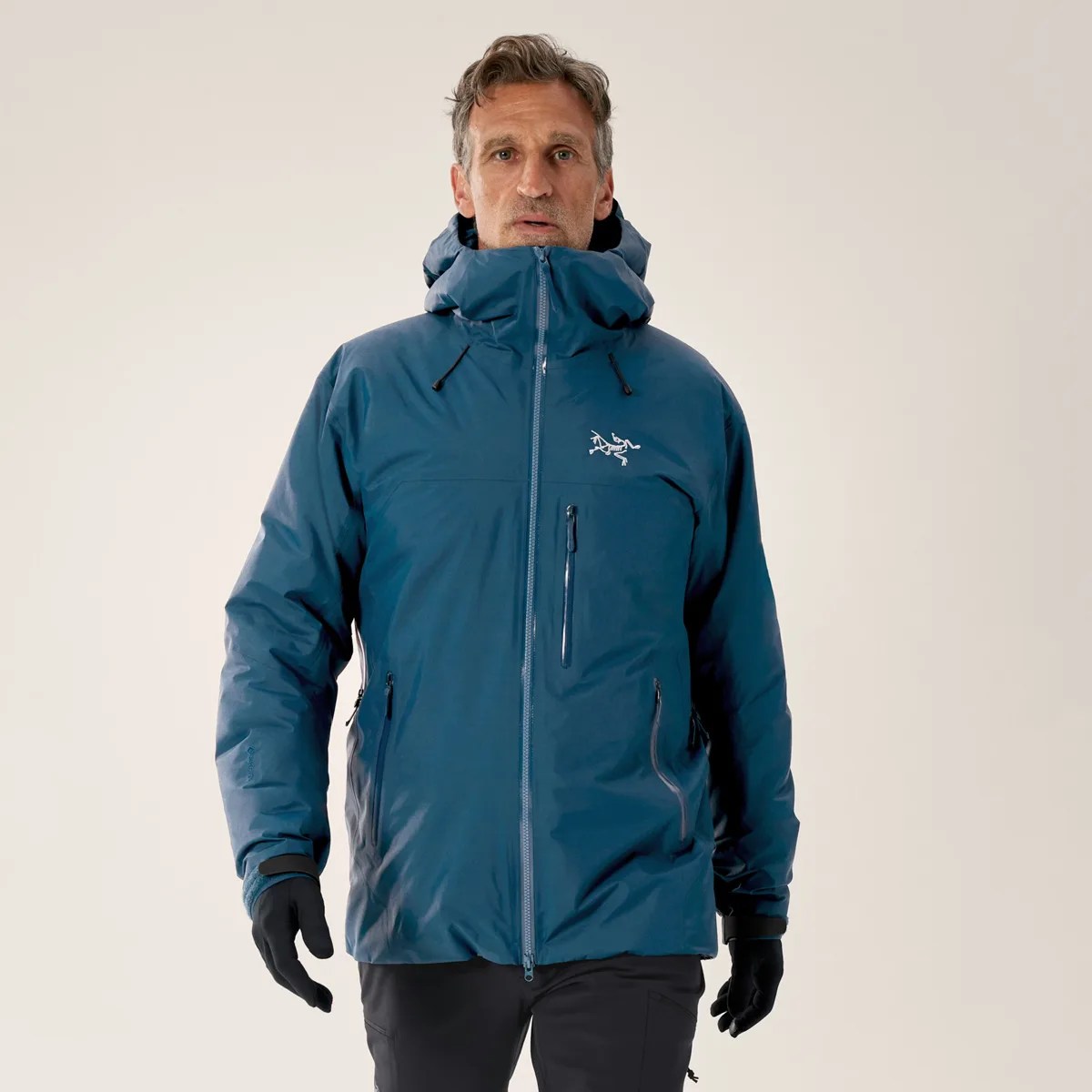 Man wearing a blue insulated hooded jacket with front zipper and zippered pockets.