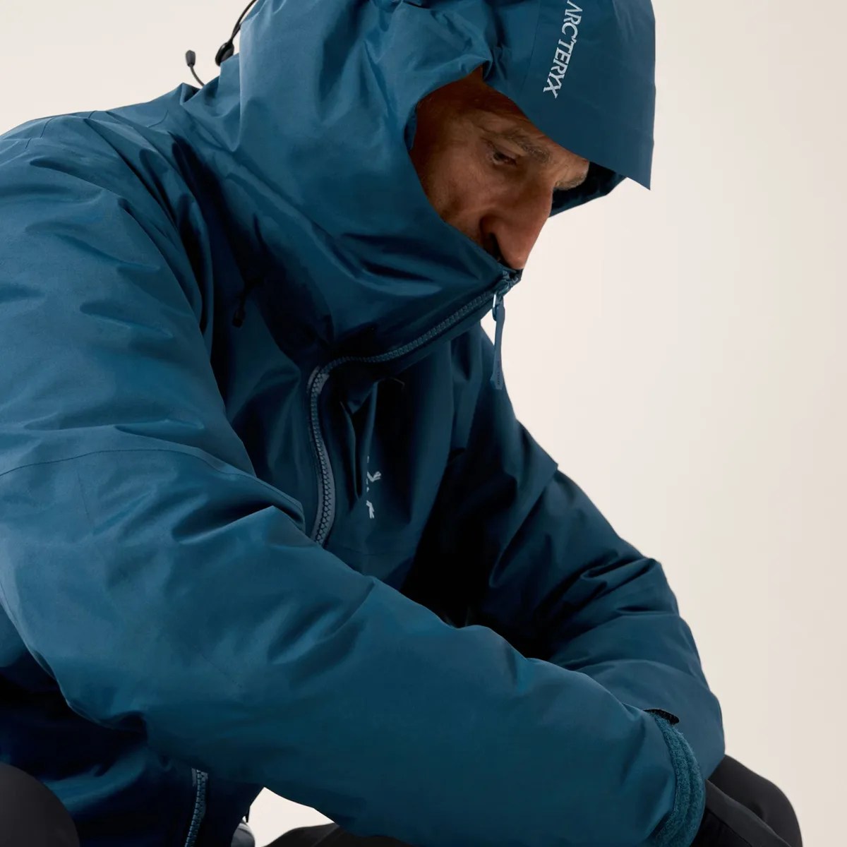 Man wearing a blue Arc'teryx hooded jacket with the hood zipped up over the chin.