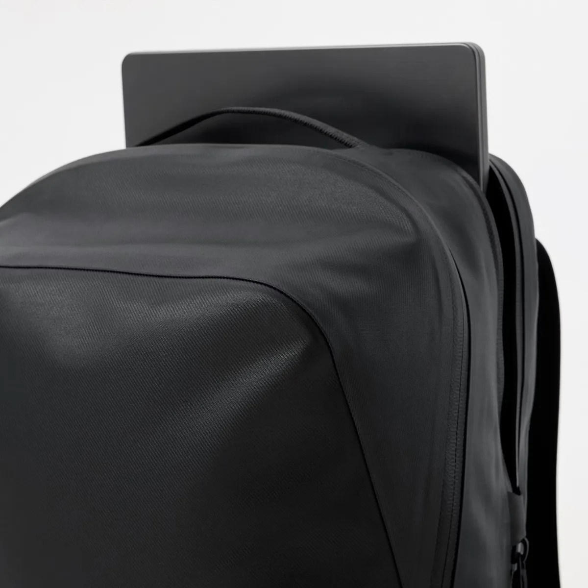 Black backpack with a laptop partially inserted into the top compartment.