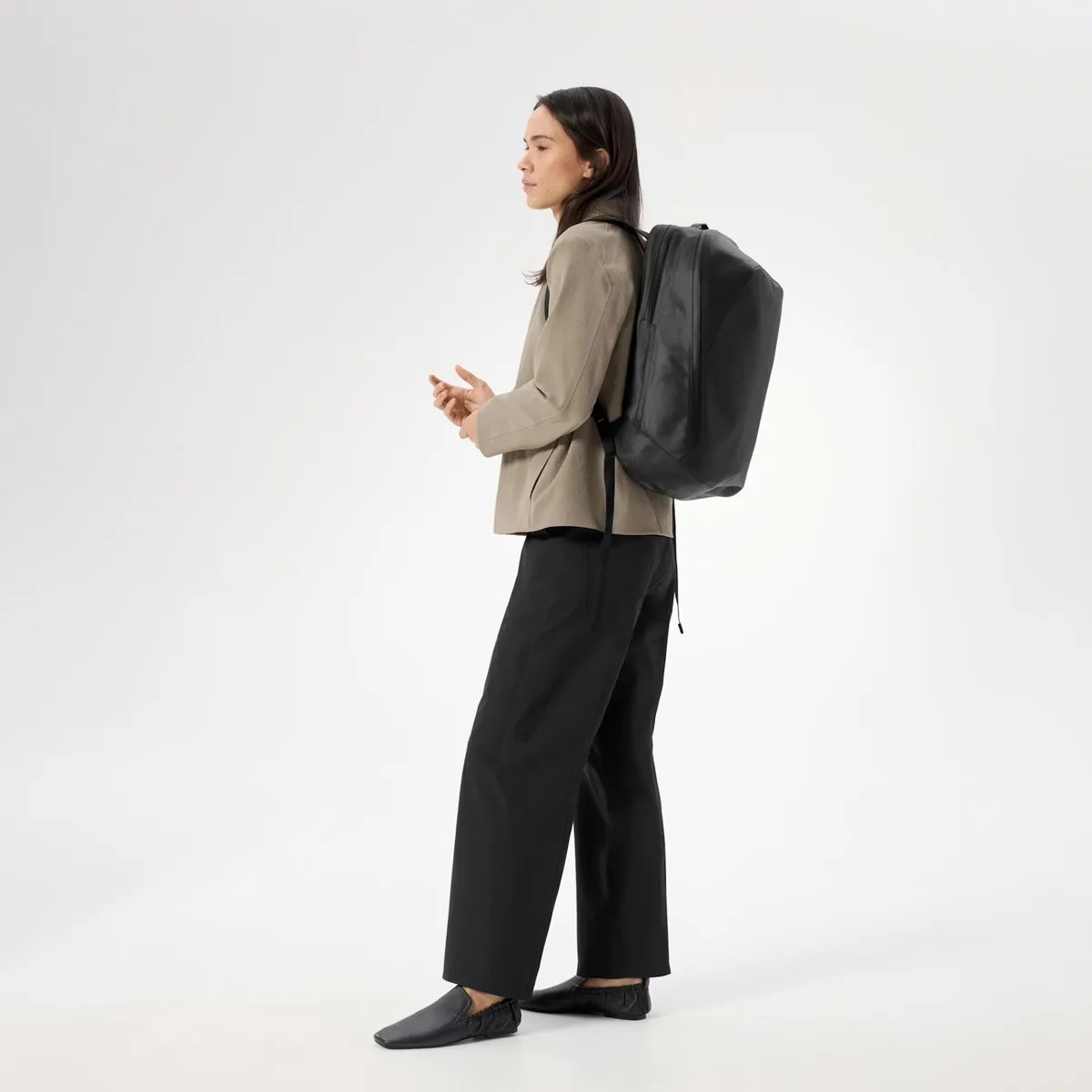 Person wearing a large black backpack with a taupe blazer, black wide-leg pants, and black slip-on shoes.