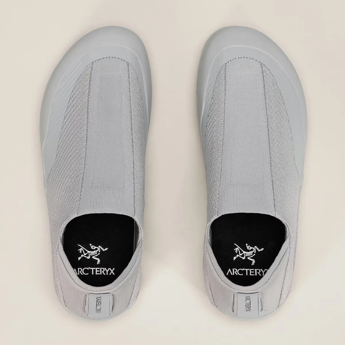 Pair of light gray slip-on shoes with black insoles featuring the Arc'teryx logo.
