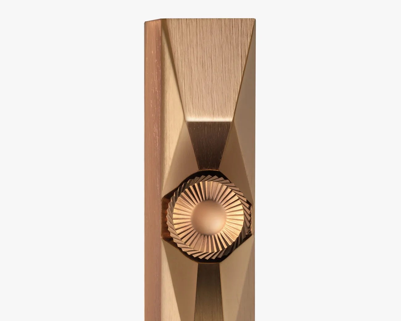 Close-up of a gold-toned metal object with a faceted surface and a central ridged circular knob.