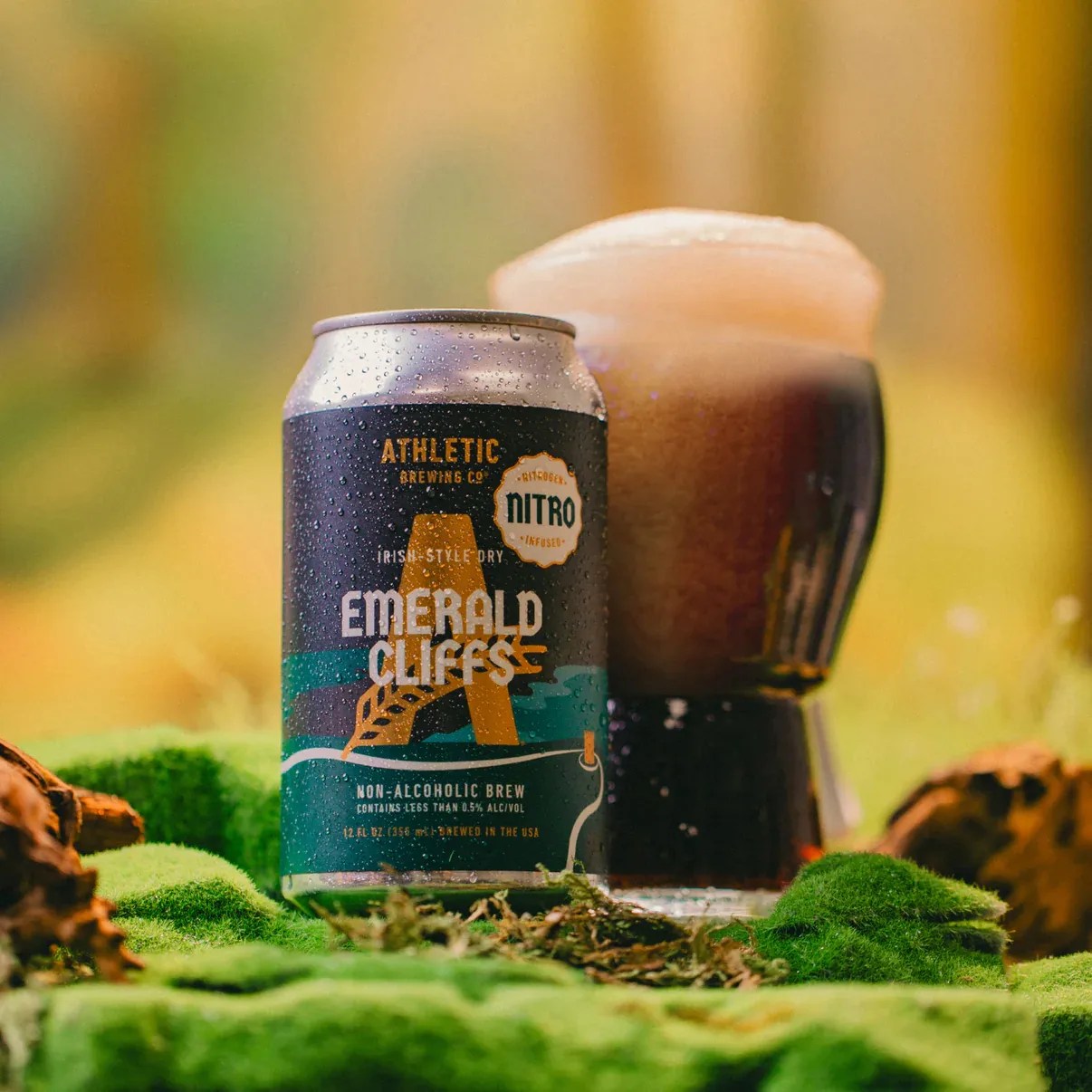 Can of Athletic Brewing Co. Emerald Cliffs non-alcoholic Irish-style dry brew with a glass of dark beer on green moss.