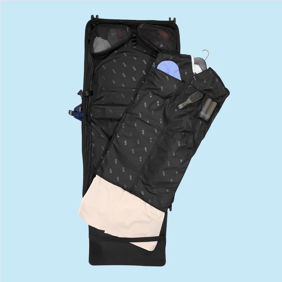 Black garment bag organizer with mesh pockets and clothes inside, laid open on a light blue background.