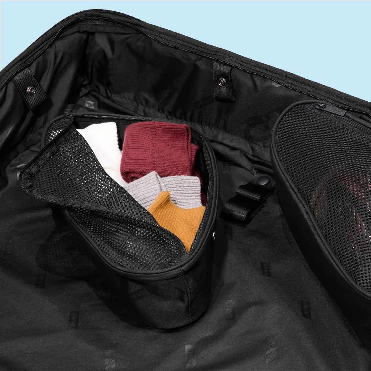 Black mesh zippered packing cube inside a black suitcase with folded colorful clothes.
