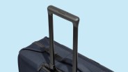 Black telescoping handle extended from navy blue fabric suitcase against a light blue background.