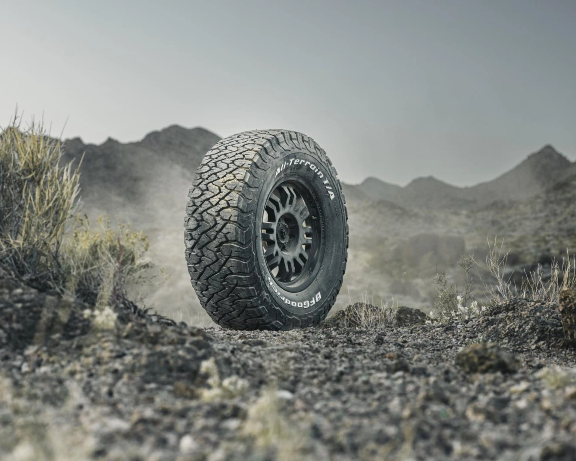 Off-road BFGoodrich All-Terrain T/A tire standing upright on rocky terrain with mountains in the background.