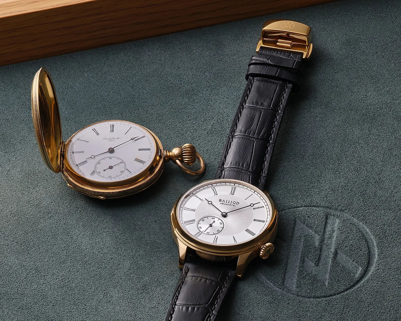 Gold pocket watch with white dial and Roman numerals next to a gold wristwatch with black leather strap on a green suede surface.