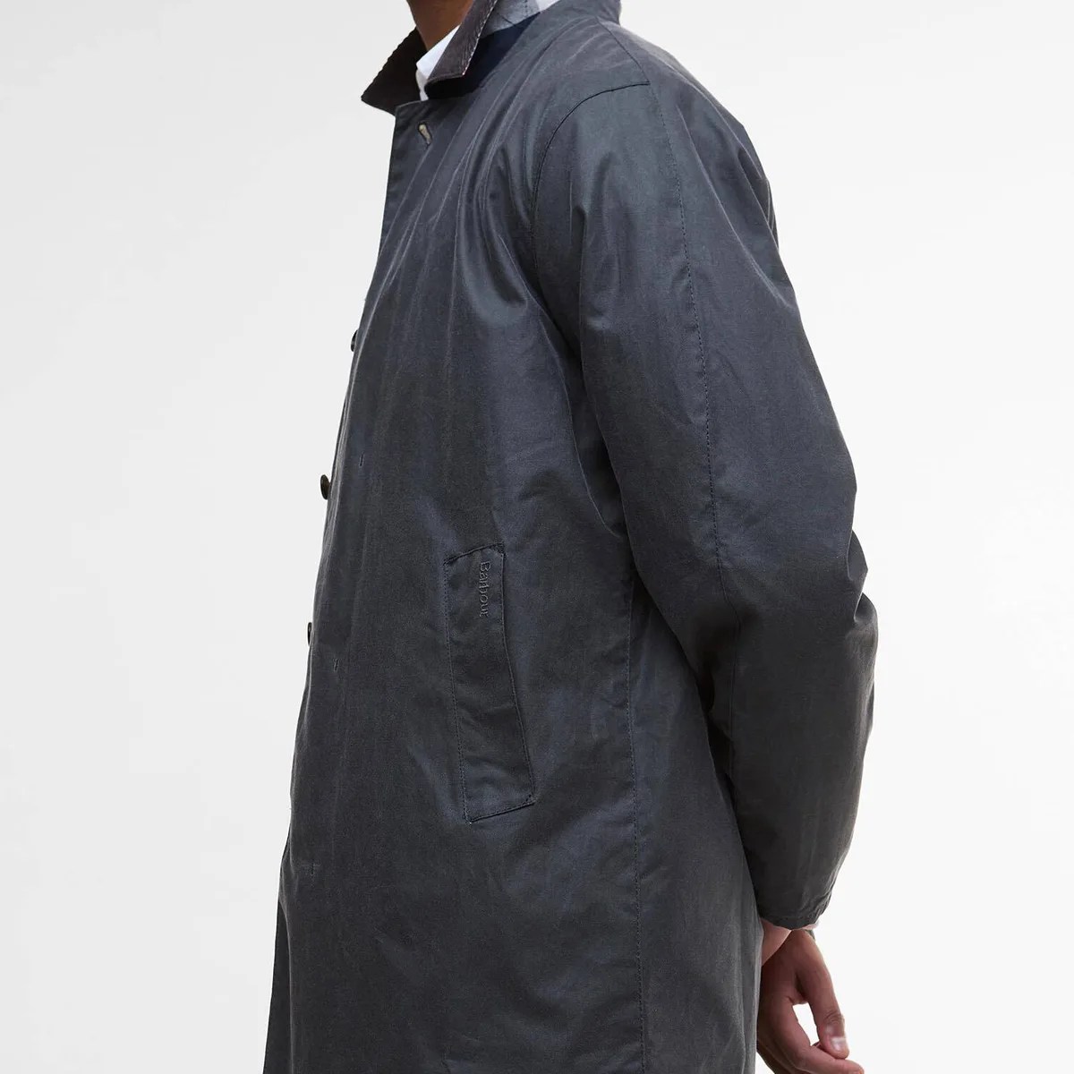Dark navy Barbour waxed cotton jacket with button closure and side pocket worn by a person.
